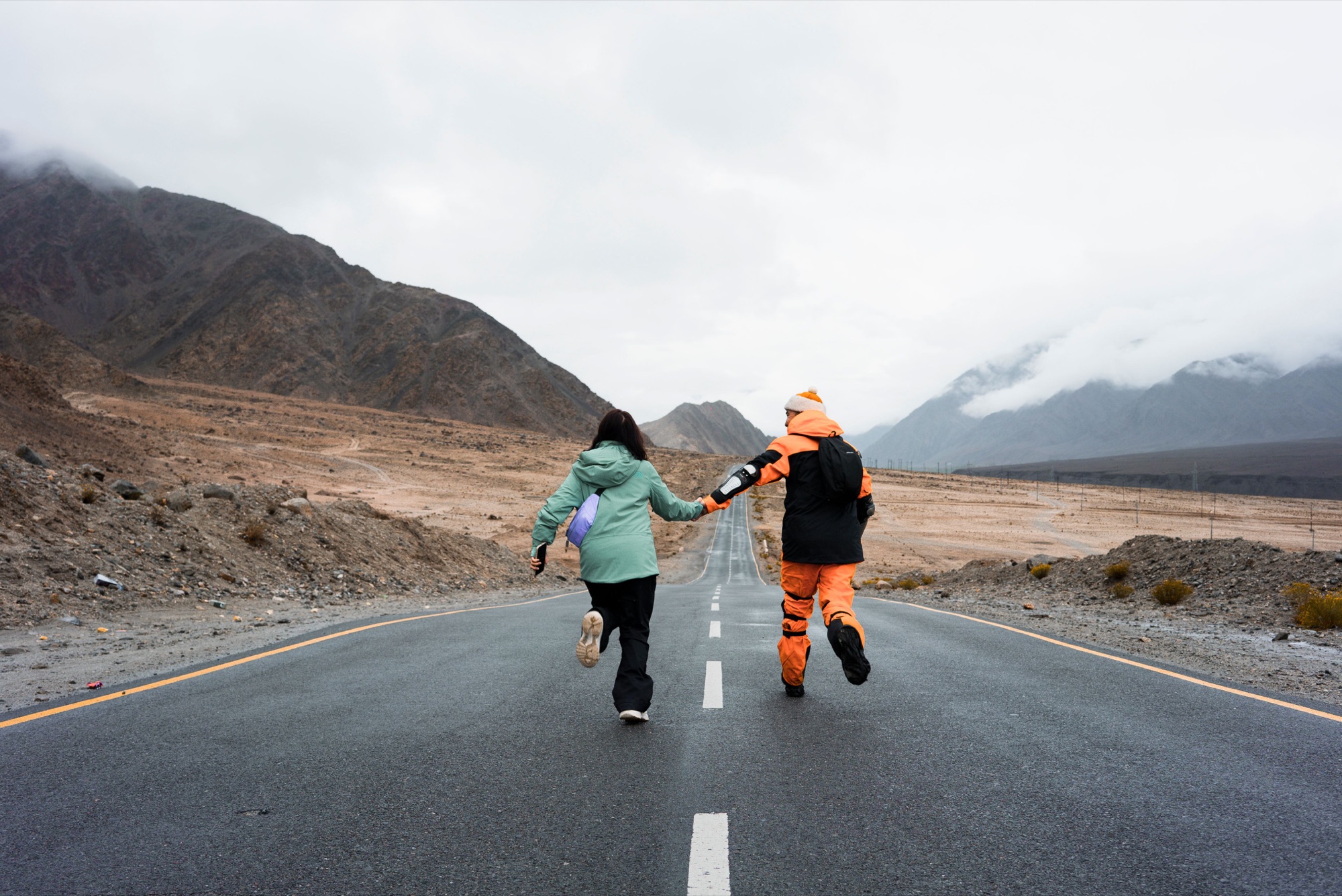 A couple running hand in hand along an open road in Ladakh